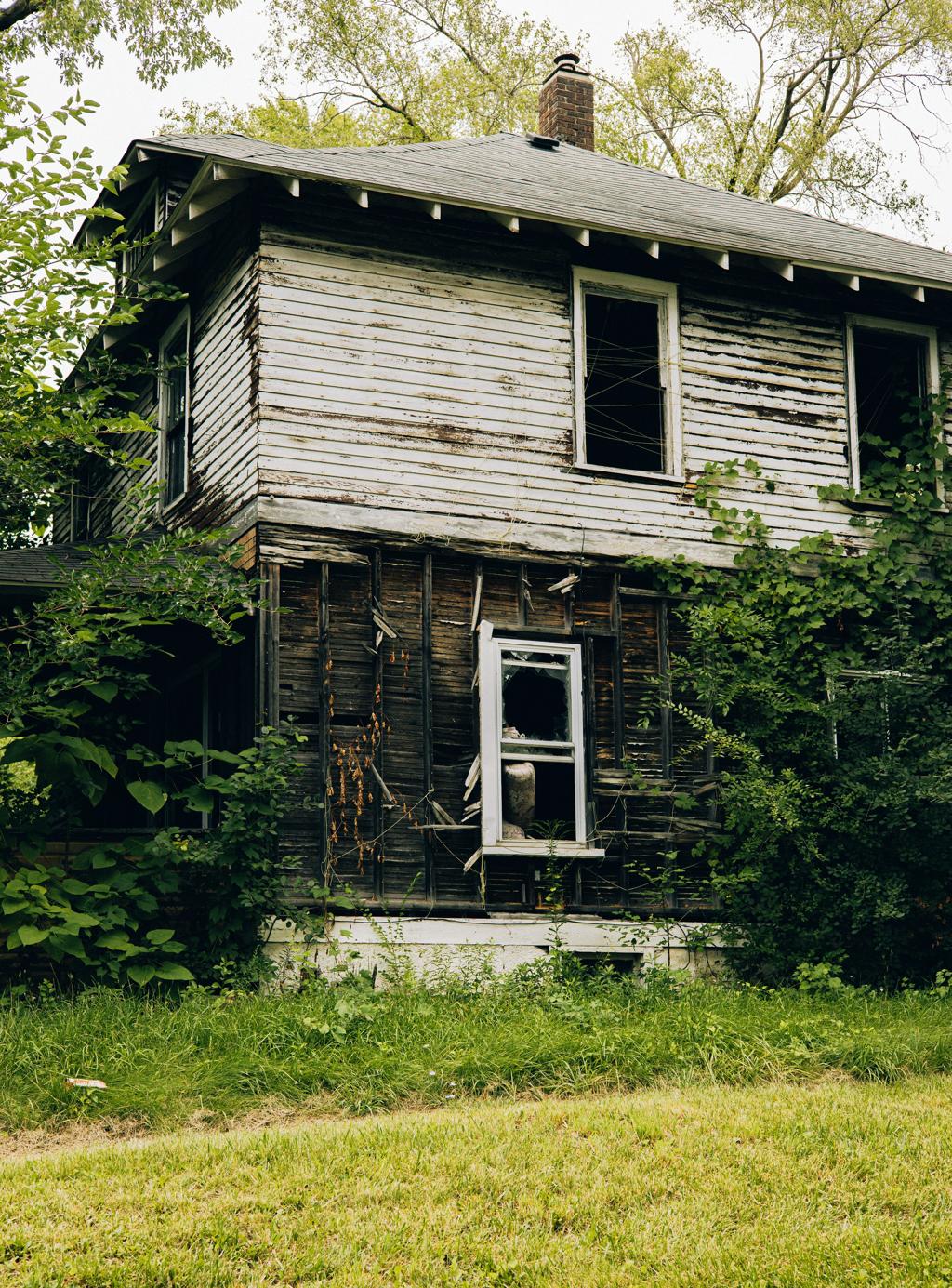 Abandoned two-story house with broken windows and overgrowth